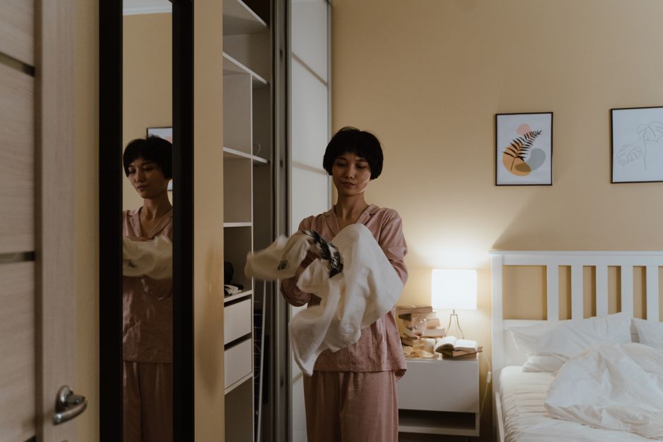 Mulher ajustando roupas no armário do quarto em uma atmosfera aconchegante e bem iluminada, ideal para temas relacionados ao cotidiano ou organização pessoal.