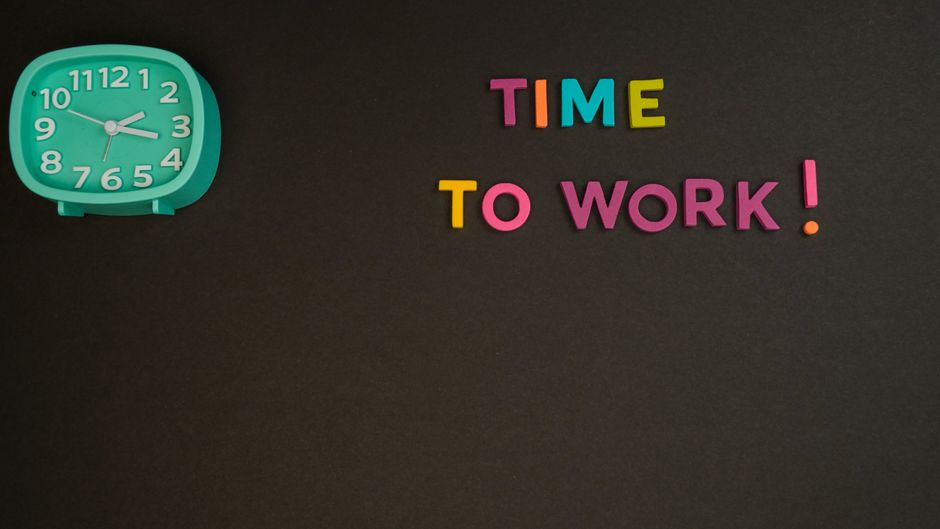 Imagem com relógio de parede e letras coloridas formando a frase 'Time to Work!', simbolizando motivação para começar a trabalhar.