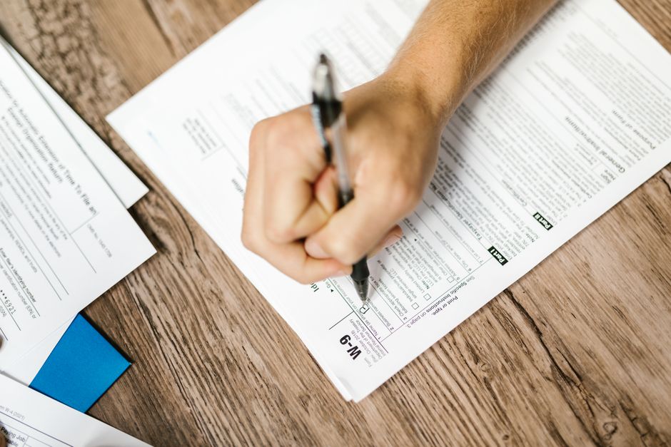 Pessoa preenchendo uma declaração de imposto de renda, representando temas de planejamento fiscal e obrigações tributárias.