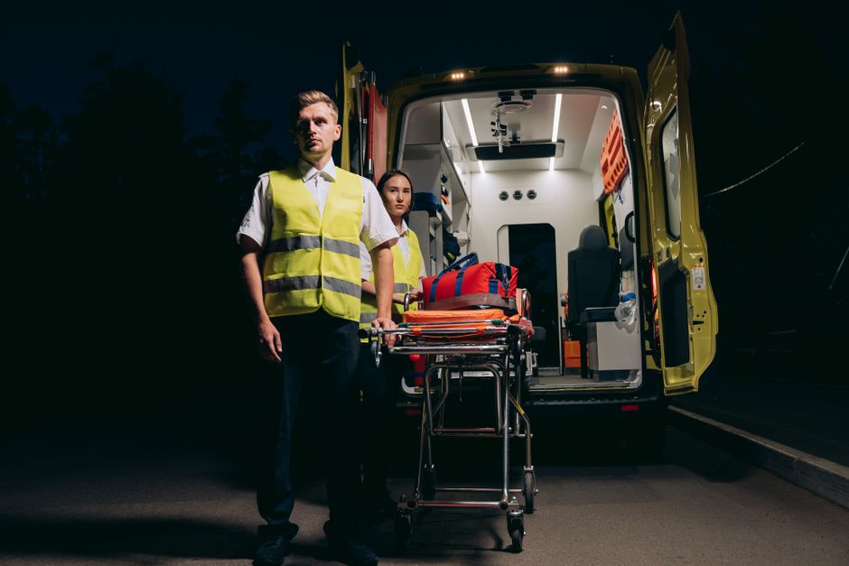 Profissionais de emergência preparando uma ambulância à noite, exemplificando o tema de serviços de saúde e urgência.