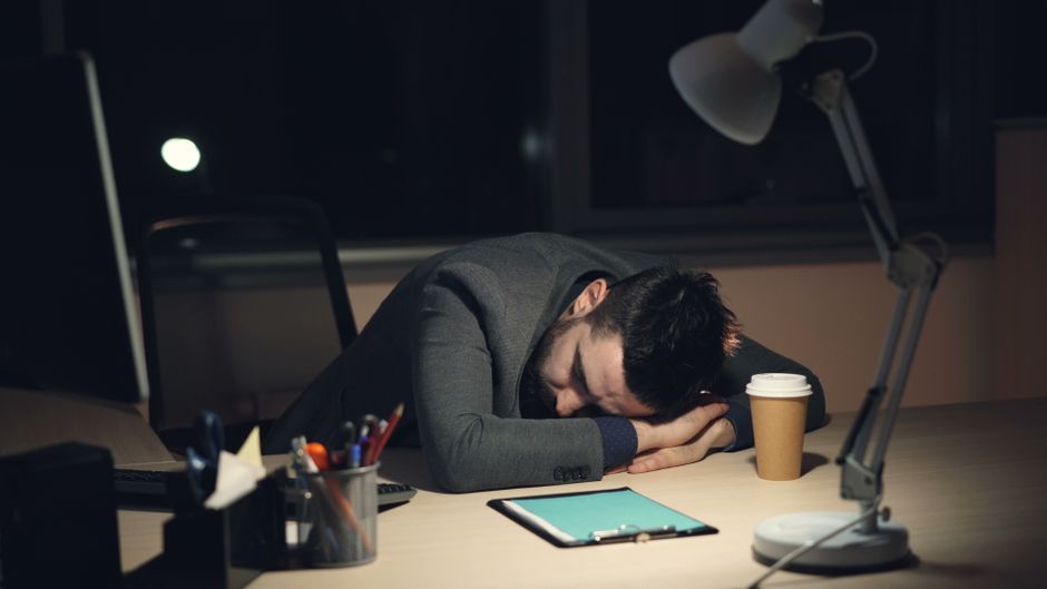 Homem cansado deitada na mesa de escritório, sugerindo fadiga ou esgotamento profissional.