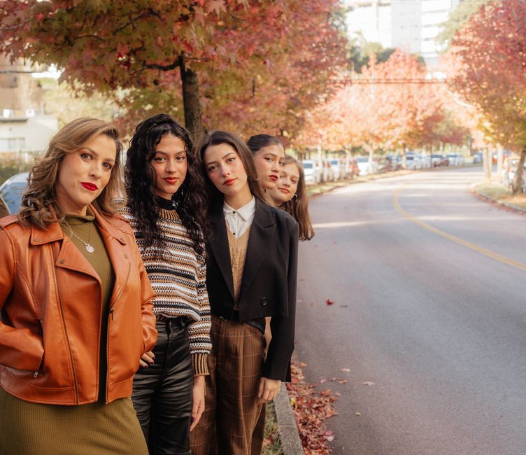 Quatro mulheres jovens posando juntas em uma rua arborizada no outono, destacando amizade e diversidade em um cenário urbano.