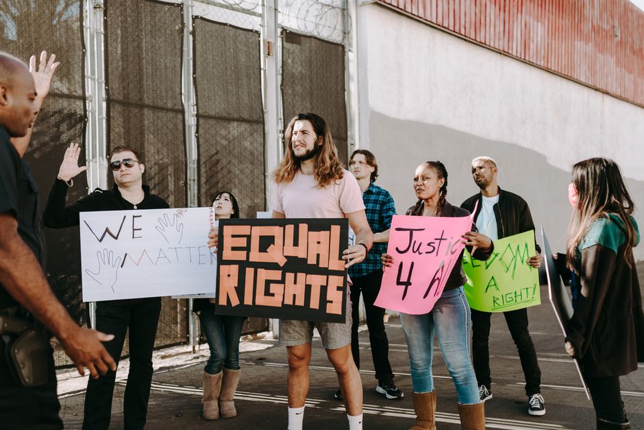 Grupo de manifestantes em uma passeata defendendo direitos iguais e justiça social, com faixas e cartazes, em um ambiente ao ar livre.