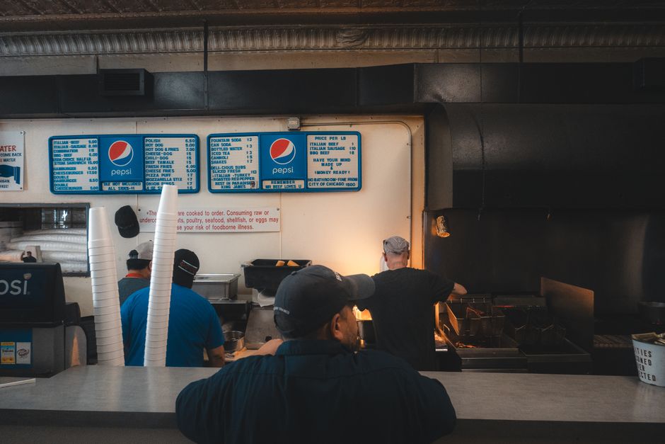 Imagem de uma lanchonete com atendentes preparando comida, ideal para artigos sobre alimentação rápida ou atendimento ao cliente.