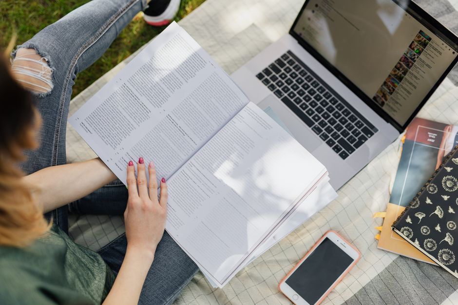 Pessoa estudando e analisando documentos e conteúdo digital ao ar livre, em um ambiente de planejamento pessoal ou acadêmico.
