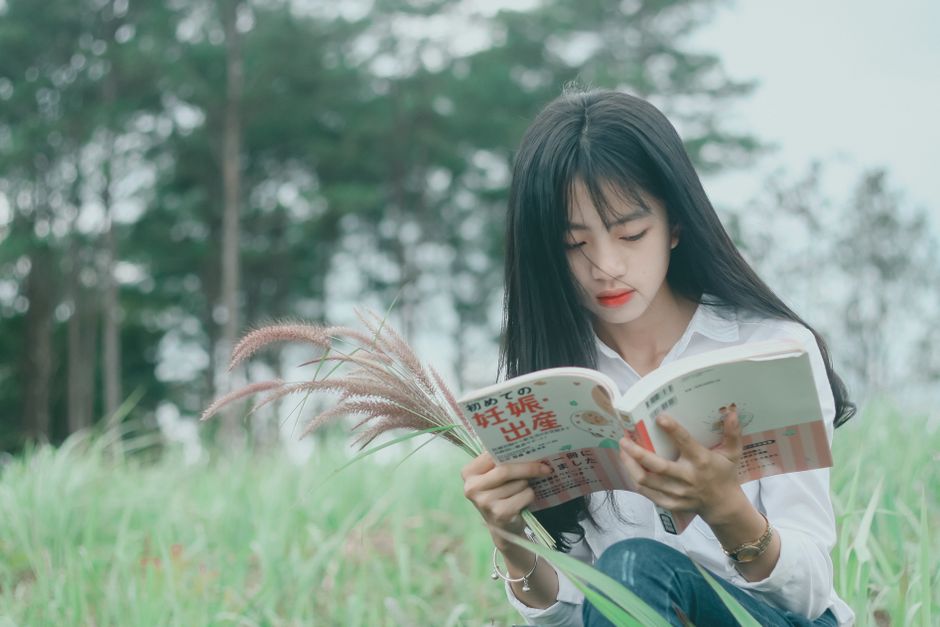 Jovem lendo um livro em um ambiente ao ar livre, cercada pela natureza, transmitindo uma sensação de tranquilidade e aprendizado ao ar livre.