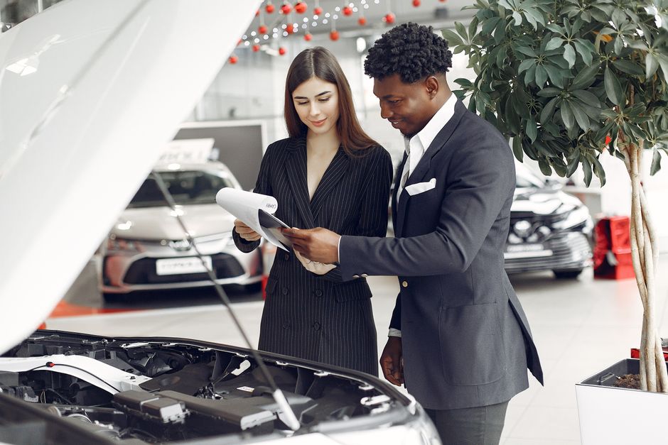 Profissional explicando detalhes técnicos de um carro para cliente em concessionária, com foco em vendas e atendimento ao cliente.