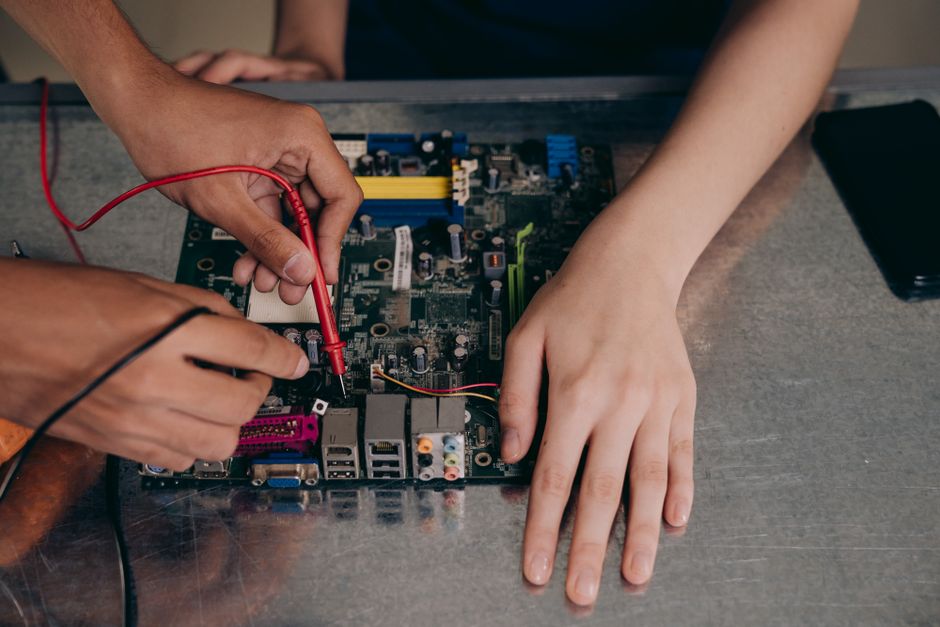 Pessoas realizando manutenção ou montagem de uma placa-mãe de computador, ilustrando tecnologia e reparo eletrônico.