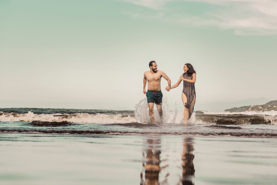 Casal feliz brincando na praia durante o pôr do sol, transmitindo momentos de lazer e conexão ao ar livre.