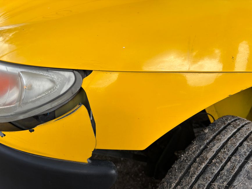Imagem de um carro amarelo com danos na frente, mostrando colisão ou acidente de trânsito.