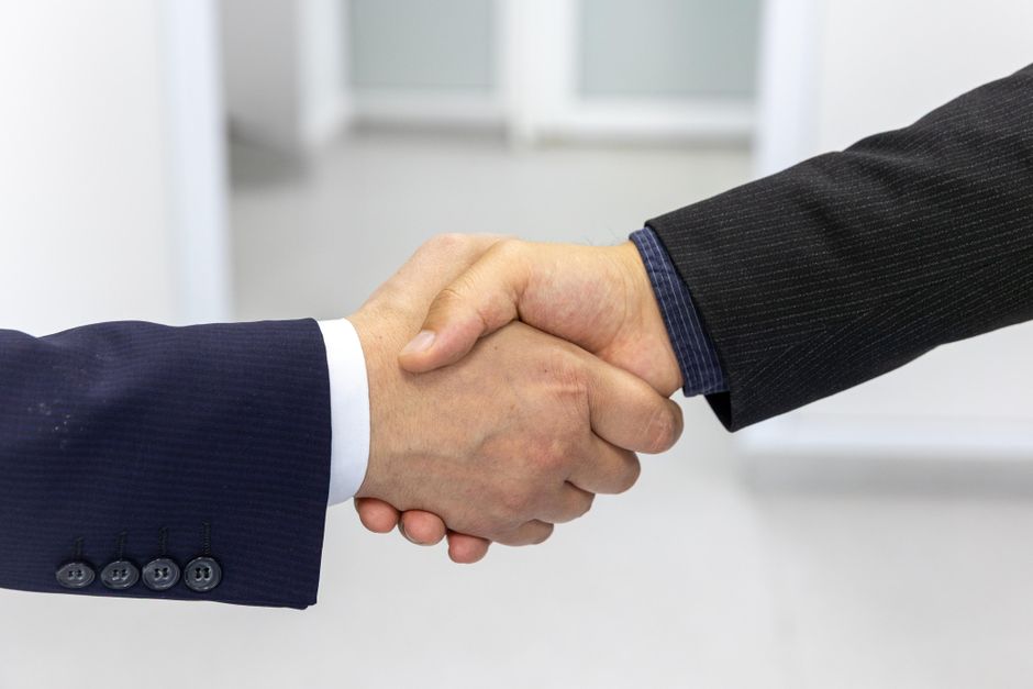 Imagem de um aperto de mãos entre duas pessoas vestidas formalmente, simbolizando acordo ou parceria de negócios.