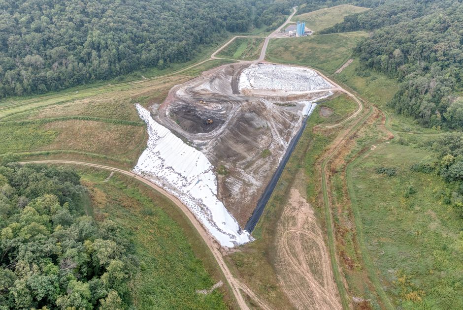 Imagem aérea de um projeto de mineração ou construção em meio a uma área verde, mostrando as operações e o levantamento de terra em atividade.