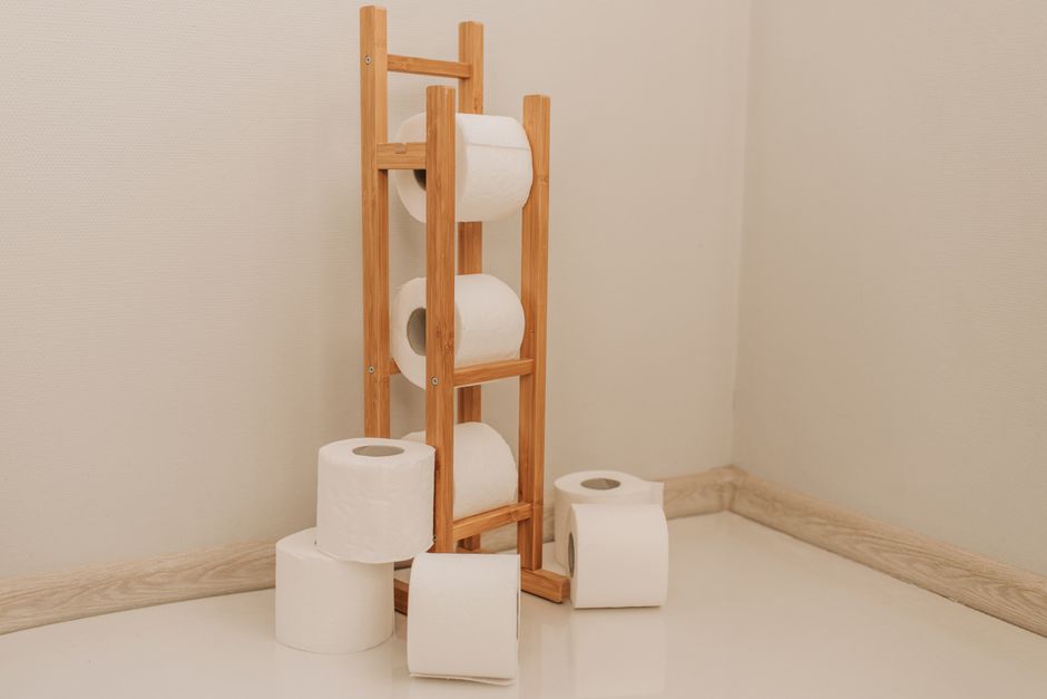 Imagem de um suporte de madeira com rolos de papel higiênico ao redor em um banheiro limpo e organizado.