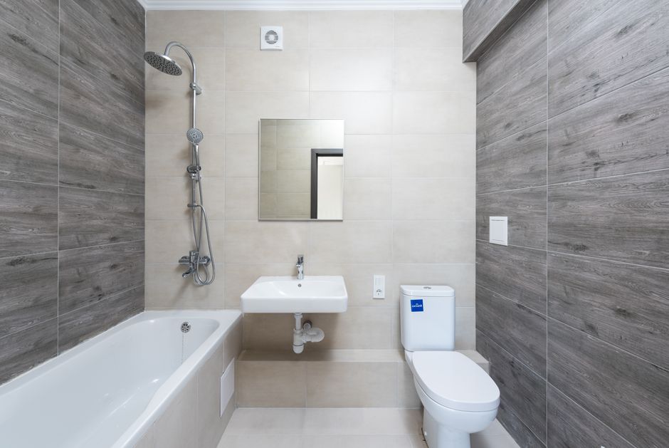 Banheiro moderno com revestimento em tons neutros, pia compacta e chuveiro com ducha manual, ideal para espaços funcionais e elegantes.
