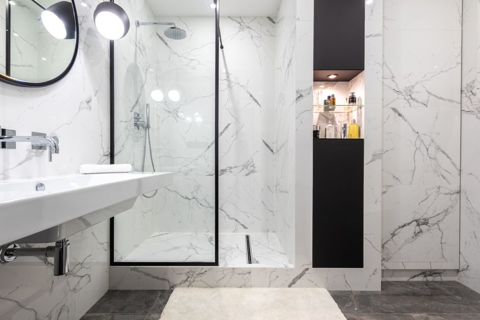 Banheiro moderno com parede de mármore, espaço de ducha com vidro e armário embutido, ideal para decoração de interiores sofisticados.