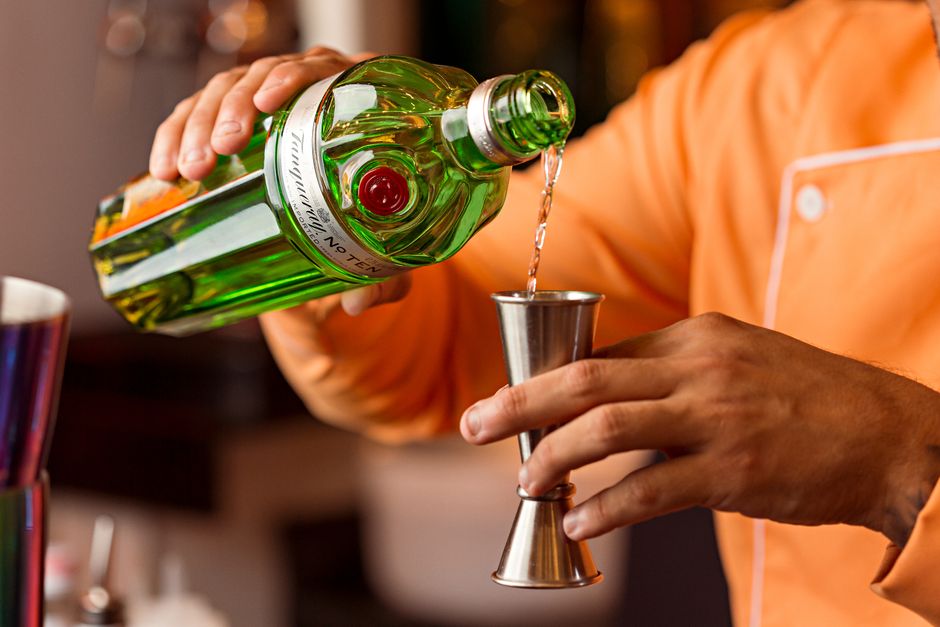 Pessoa preparando um drink com cuidado em um ambiente de bar ou convivência social.