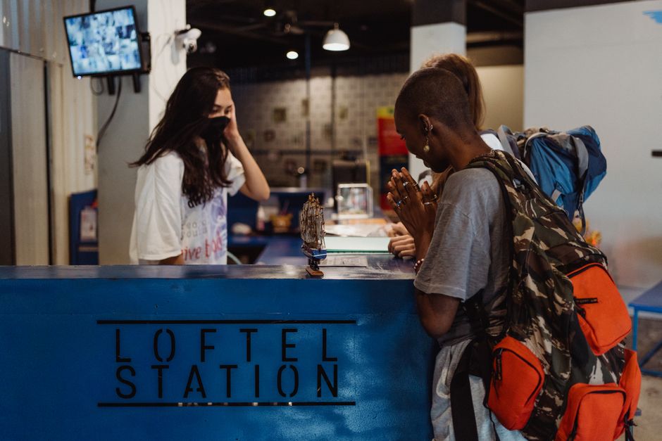 Mochileiros fazendo check-in na recepção de um hostel, aguardando o processo de hospedagem.