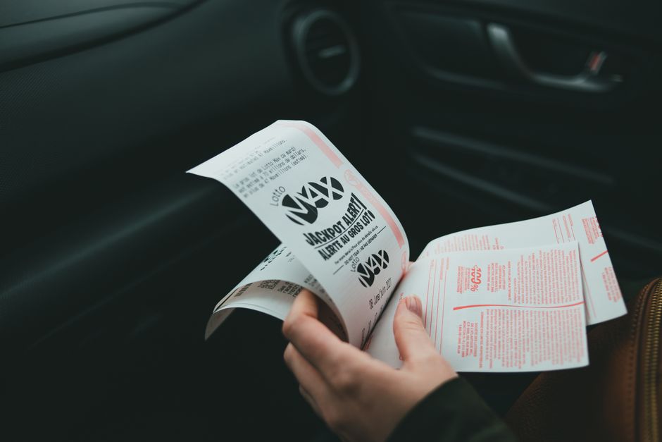 Pessoa segurando bilhetes de loteria dentro de um carro, sugerindo esperança ou sorte em viagem.