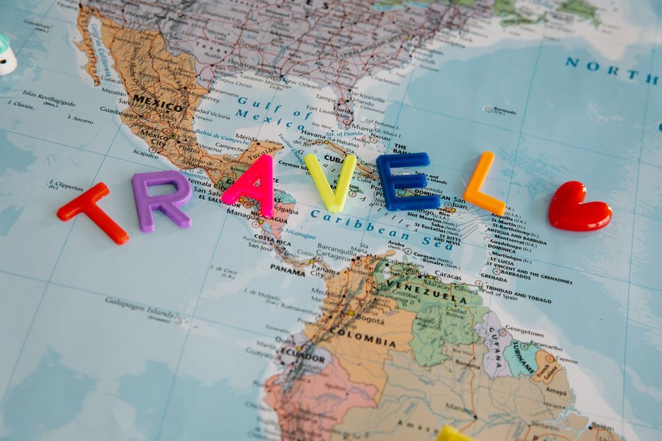 Mapa mundial com a palavra 'TRAVEL' formada por letras coloridas e uma coração ao final, simbolizando o tema de viagem e aventura internacional.
