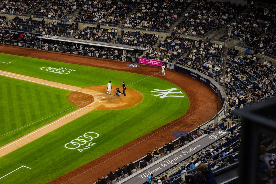 Imagem de um estádio de beisebol em evento esportivo com jogadores e torcida presente.