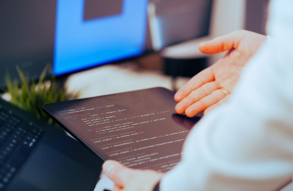 Pessoa utilizando um tablet para programação ou análise de dados em um ambiente de trabalho digital.