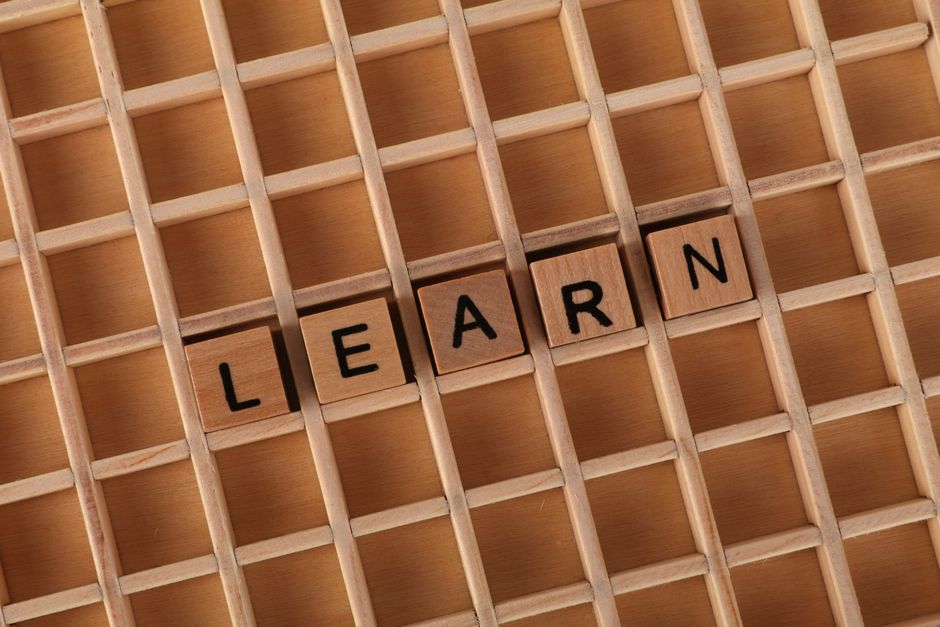 Imagem de palavras cruzadas com blocos de madeira formando a palavra 'LEARN', representando o tema de aprendizagem e desenvolvimento.
