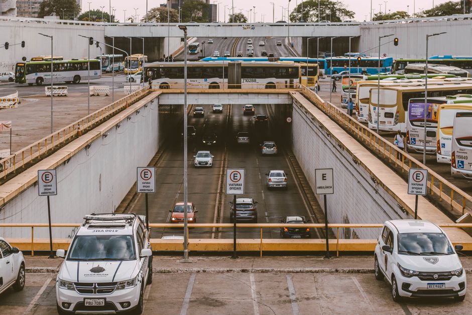 Estacionamento subterrâneo em um centro urbano com entrada de veículos, cercado por ônibus e carros, em um cenário de mobilidade urbana.