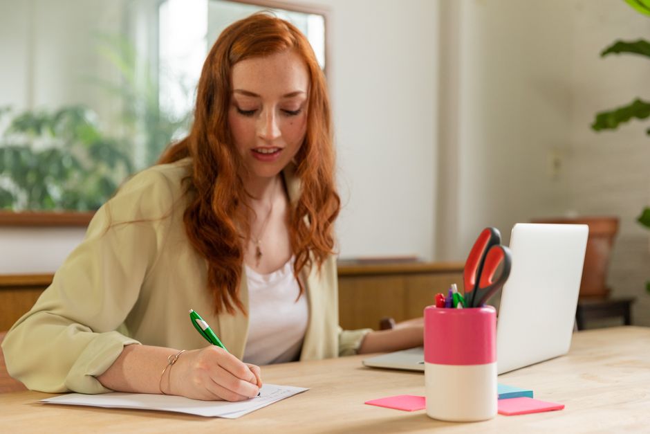 Mulher trabalhando de forma produtiva em ambiente de escritório com materiais de escrita e computador acessíveis.