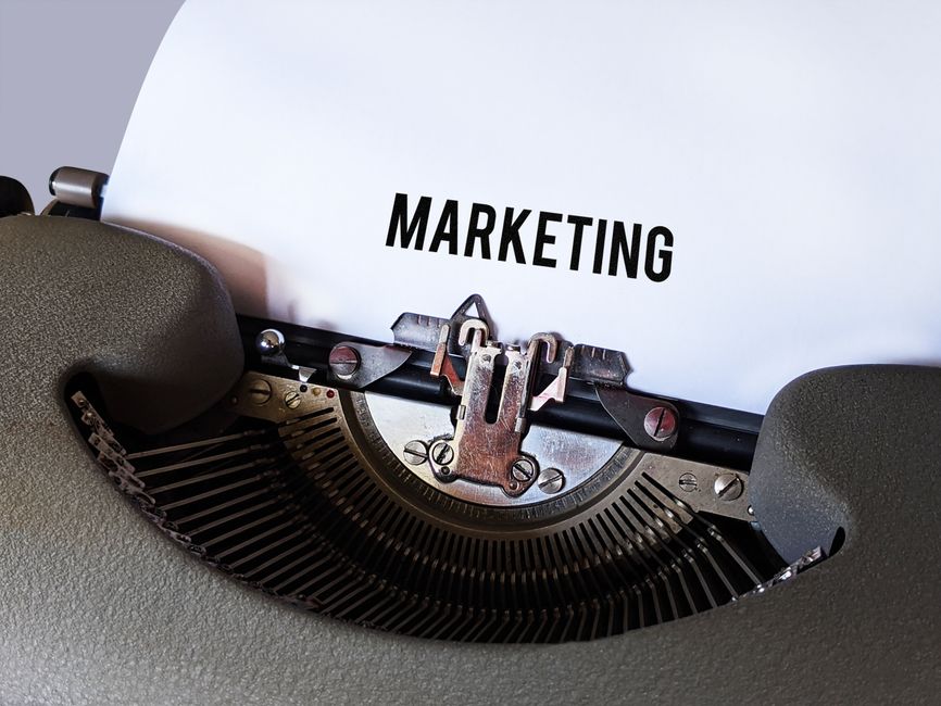 Máquina de escrever antiga exibindo a palavra 'MARKETING' em uma folha de papel, simbolizando estratégias tradicionais de divulgação e publicidade.