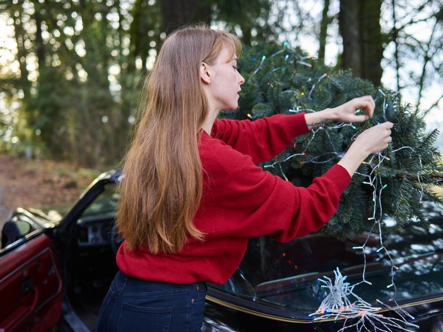 Mulher decorando uma árvore de Natal ao ar livre, refletindo a preparação para festividades de fim de ano.