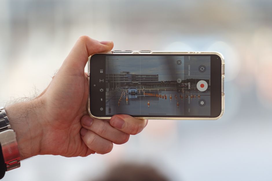 Pessoa gravando uma cena urbana ao ar livre com um smartphone, destacando a captura de conteúdo visual em ambiente externo.