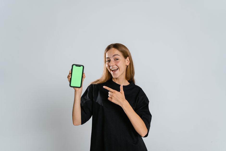 Jovem sorridente apontando para um smartphone com tela verde, representando inovação e tecnologia digital.