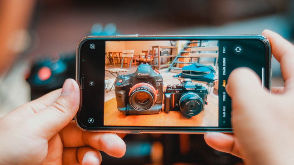 Imagem que mostra uma pessoa tirando uma foto de câmeras digitais e acessórios em uma mesa, focando na captura de equipamentos fotográficos.