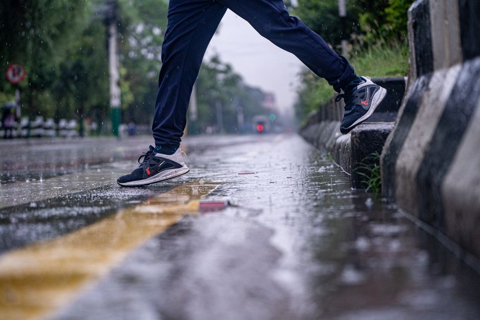 Pessoa tentando atravessar uma rua chuvosa, evidenciando a dificuldade de lidar com dias de chuva intensa.