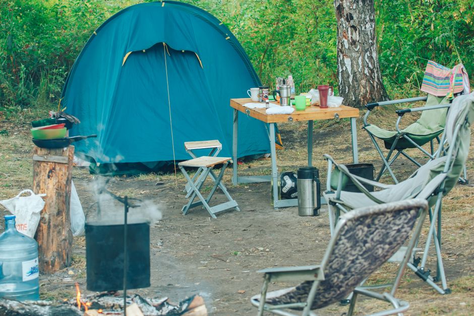Cena de acampamento ao ar livre com barraca, cadeiras e uma fogueira, ideal para artigos sobre lazer na natureza e aventuras ao ar livre.