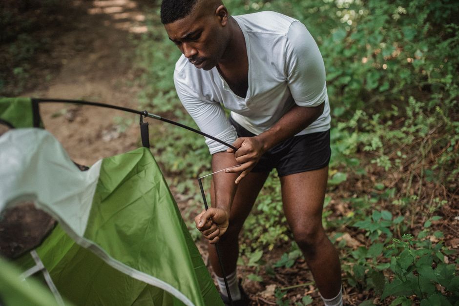 Homem preparando uma barraca de acampamento na floresta, demonstrando atividades ao ar livre e camping.