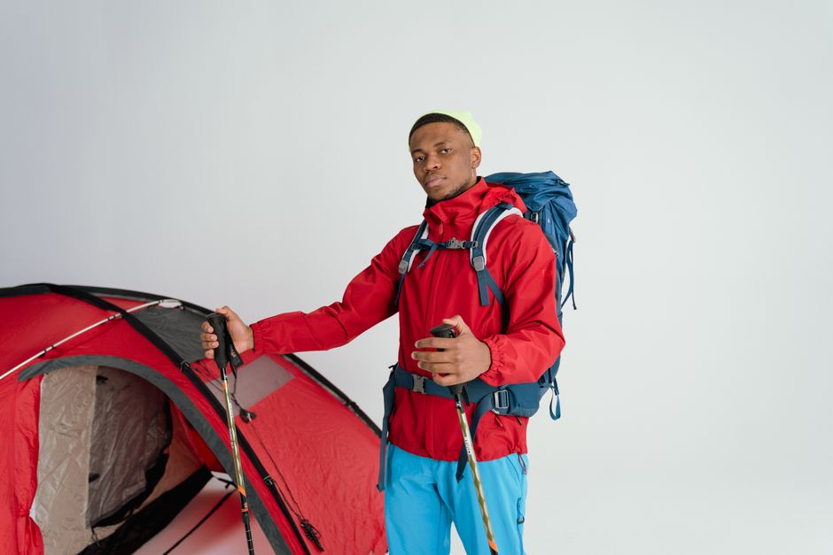 Jovem aventureiro com mochila diante de uma barraca de camping, pronto para explorar a natureza.