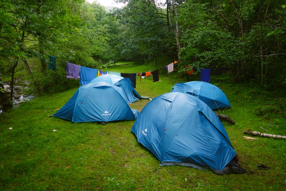 Imagens de acampamento em meio à floresta, com tendas azuis e roupas secando em uma corda ao ar livre.