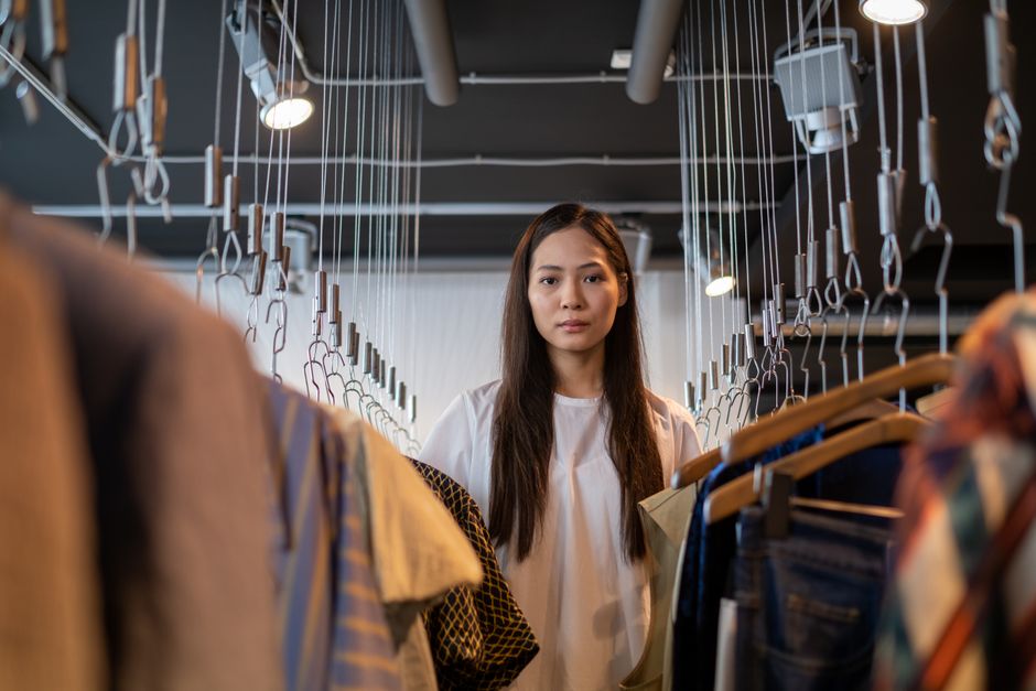 Mulher examinando roupas em uma loja de roupas, representando escolhas de consumo e moda.