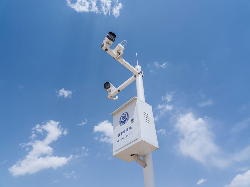 Câmeras de vigilância instaladas em uma estrutura ao ar livre sob um céu azul com nuvens, simbolizando segurança e monitoramento urbano.