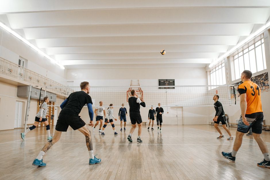 Grupo de pessoas jogando vôlei em uma quadra de ginásio moderna com iluminação natural e ambiente esportivo.
