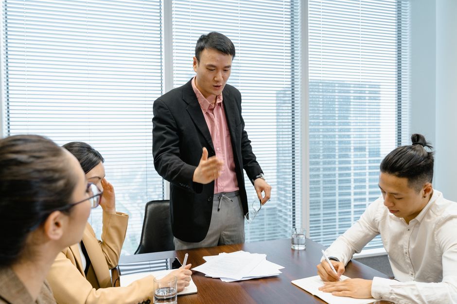 Homem liderando uma reunião de equipe em um ambiente de escritório, abordando questões de negócios e estratégias.