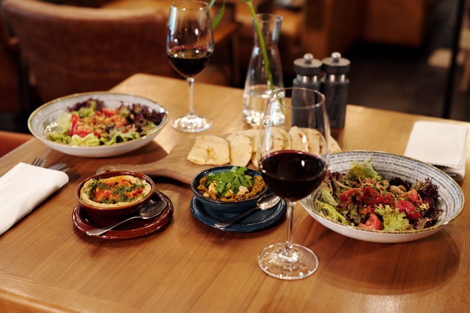 Mesa de jantar com saladas, pratos quentes e duas taças de vinho, ideal para um momento de convivência e gastronomia.