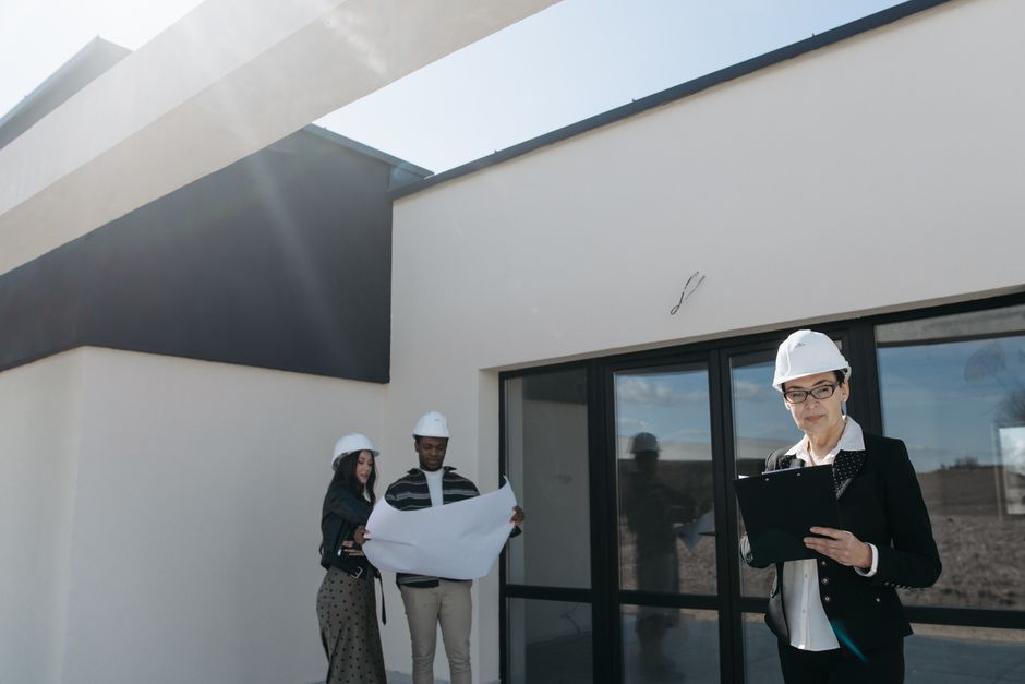 Profissional de arquitetura ou engenheira supervisionando uma construção residencial com equipe ao fundo, em um ambiente externo e moderno.