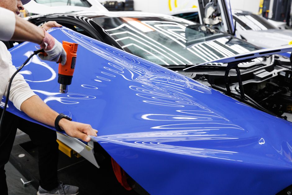 Pessoa aplicando pintura ou adesivo em carro de corrida em ambiente de fábrica ou oficina colaborativa.