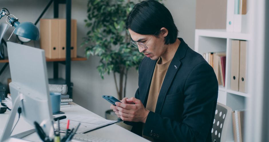 Homem em ambiente de trabalho usando smartphone, refletindo sobre produtividade ou comunicação empresarial.
