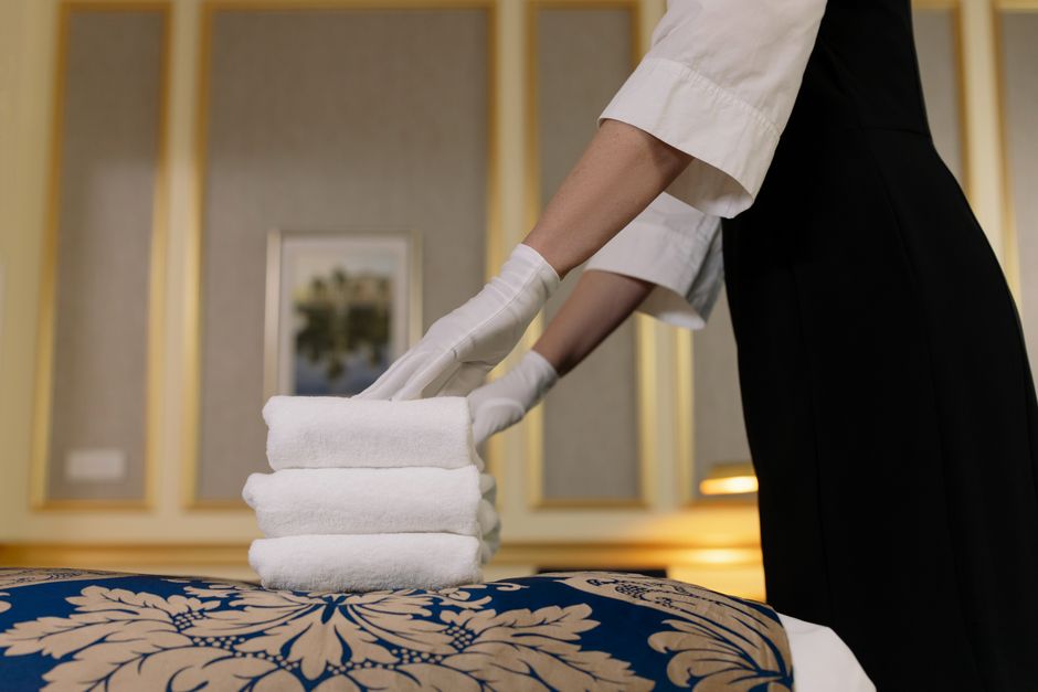 Profissional de hotelaria organizando toalhas em uma cama, simbolizando serviços de hospitalidade e acomodação de alta qualidade.