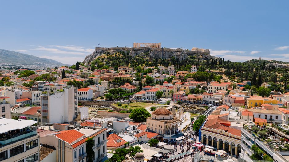 Vista panorâmica do centro histórico de Atenas com a Acrópole ao fundo, destacando a combinação de arquitetura antiga e moderna em uma cidade vibrante.
