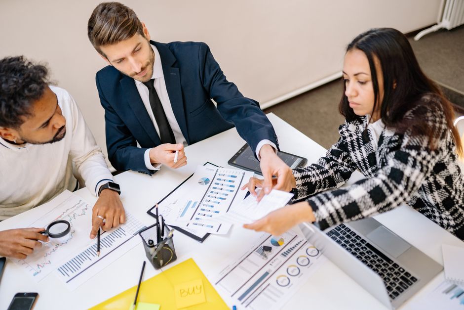 Três profissionais reunidos em uma reunião de negócios, analisando relatórios e discutindo estratégias com foco em planejamento financeiro ou gestão empresarial.