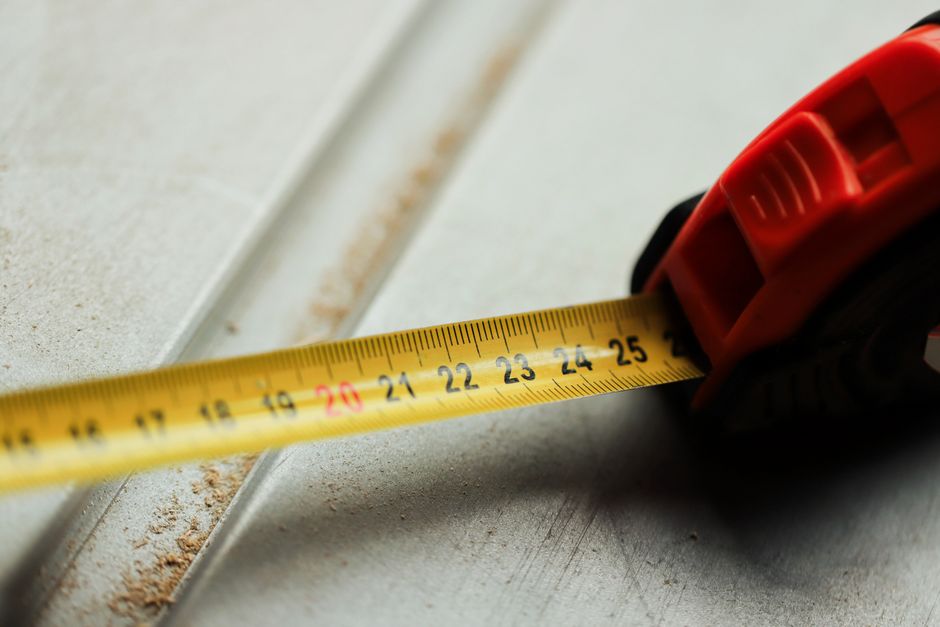 Ferramenta de fita métrica sendo usada para medir a largura de uma superfície de cerâmica, ilustrando precisão e planejamento em projetos de construção ou reforma.